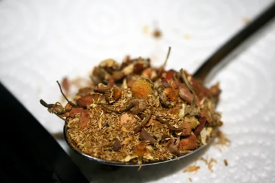 A spoonful of loose chamomile tea with dried apple and cinnamon pieces mixed in.