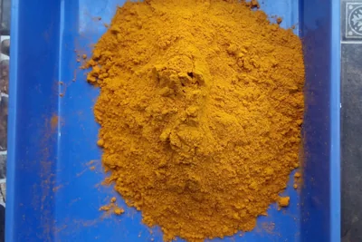 Orange turmeric powder heaped in a blue plastic tray on a tiled floor.