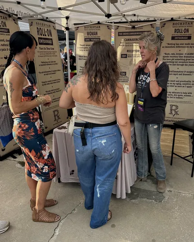 Heather Reilly Hiemstra talks with two women in front of her booth's banners, wearing a Cannadelic vendor badge on a lanyard.