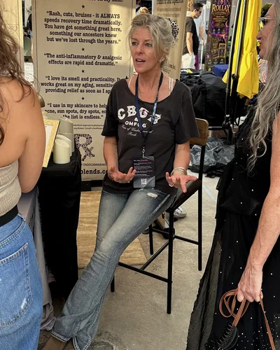 Heather Reilly Hiemstra sits on a tall stool and talks with two women, a banner of printed testimonials behind her.